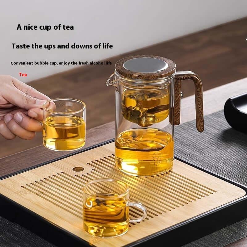 A transparent teapot on a wooden tray with a cup of tea, showcasing elegance and function in tea brewing.