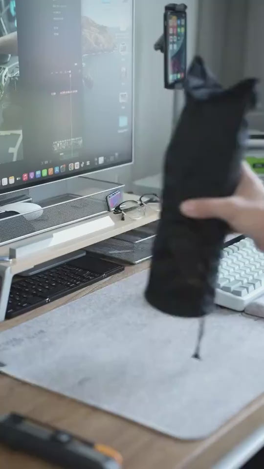 Person holding a black product near a computer setup with a keyboard and monitor.