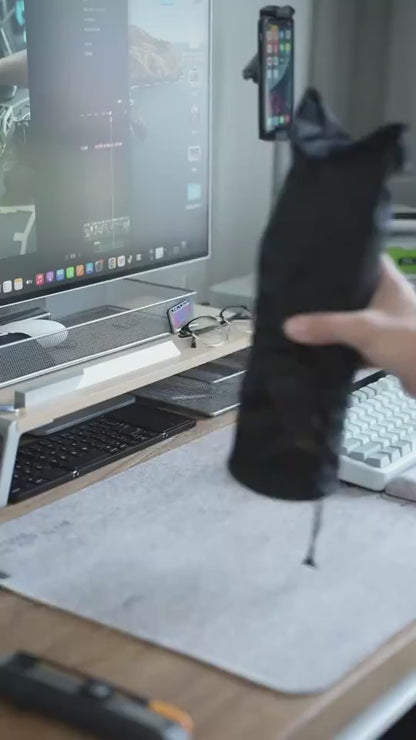 Person holding a black product near a computer setup with a keyboard and monitor.
